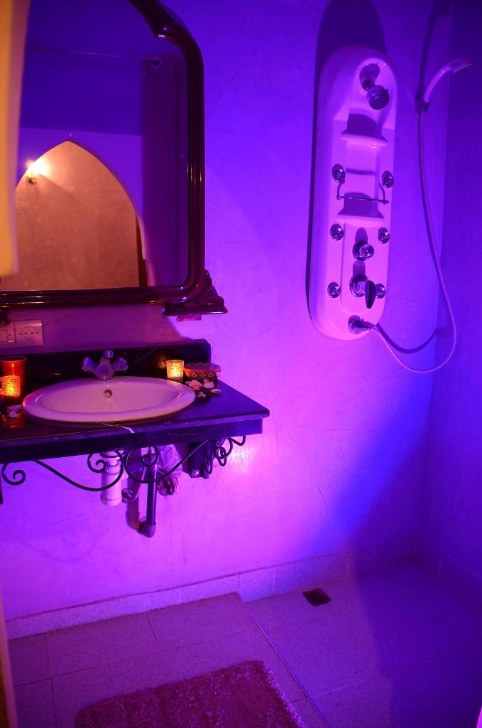 La salle de bains est pourvue d'un lavabo et d'un miroir éclairé par une lumière violette. dans l'établissement Dar LEULEU, à Marrakech