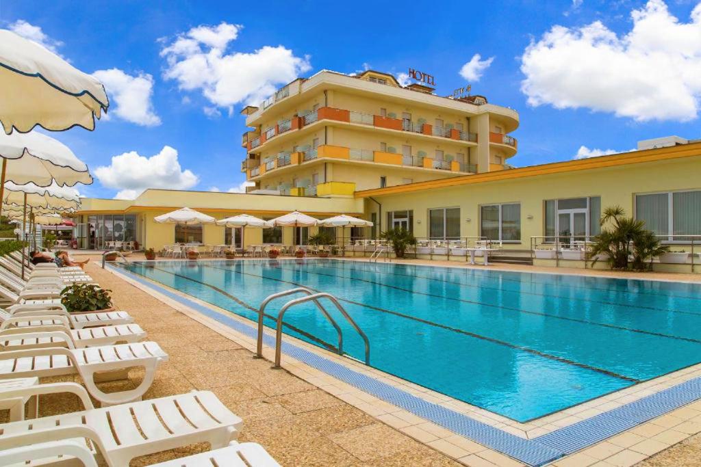 une piscine avec des chaises longues blanches et un hôtel dans l'établissement Hotel Mara, à Ortona