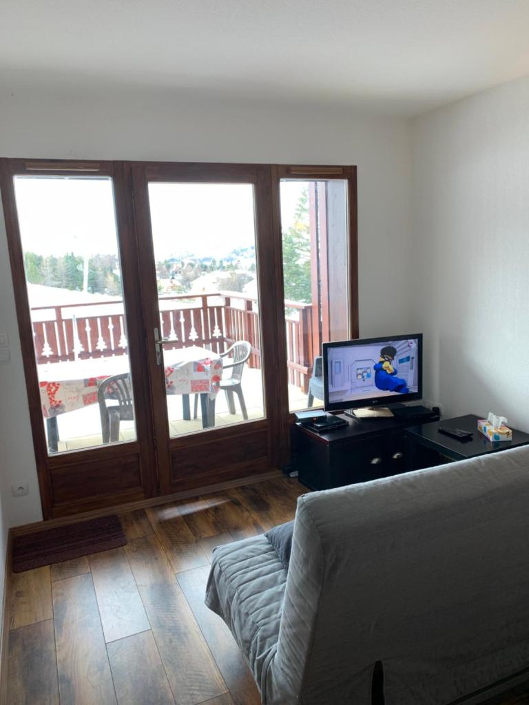 un salon avec un canapé et une télévision et un balcon dans l'établissement l'appart sur les pistes, à Saint-Étienne-en-Dévoluy