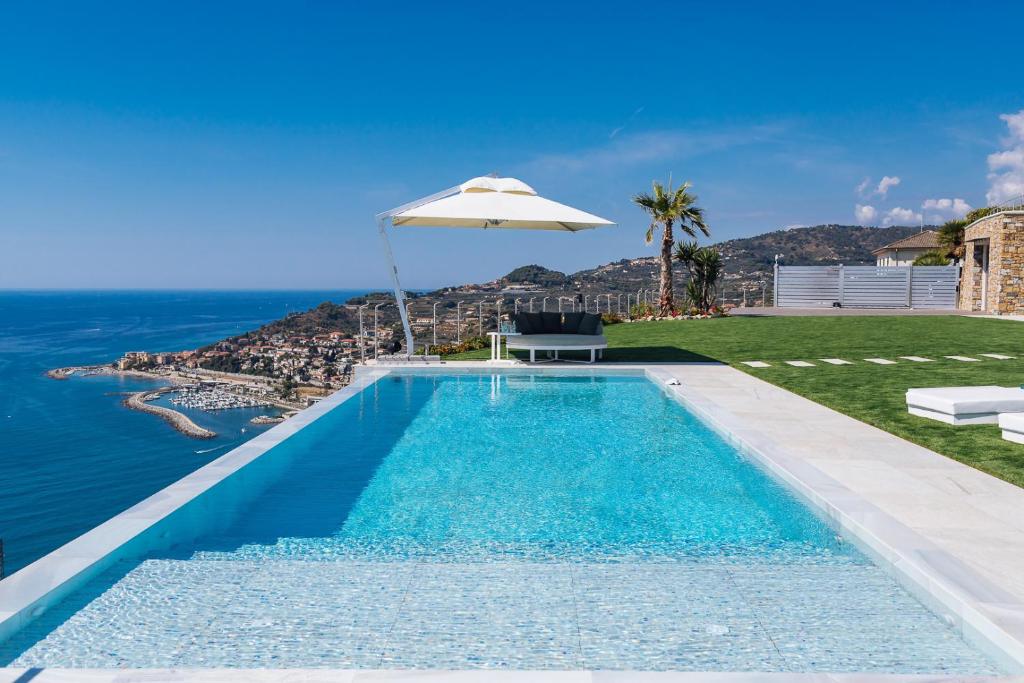 - une piscine avec un parasol et l'océan dans l'établissement Villa Sabrina Riviera dei Fiori a Picco sul Mare con Piscina Privata ,WELLNESS & SPA, à Imperia