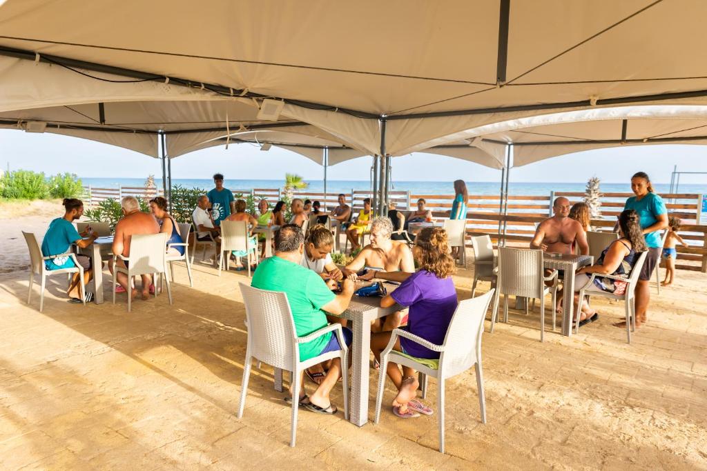 un groupe de personnes assises à des tables sous un parasol sur la plage dans l'établissement Triscinamare Hotel Residence, à Triscina