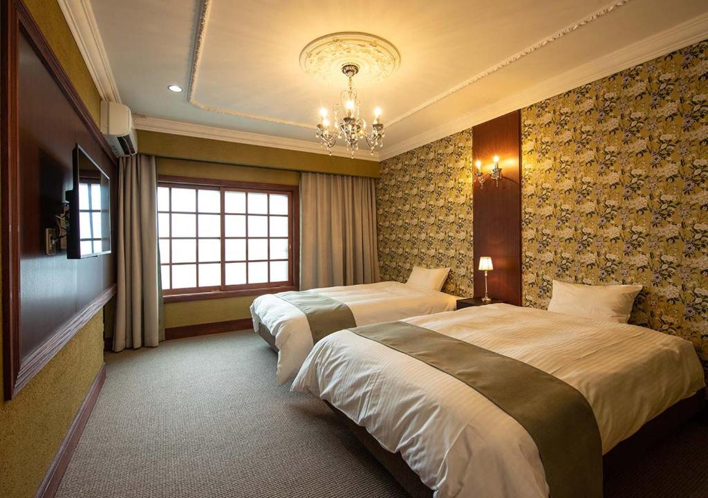 Cette chambre comprend deux lits et un lustre. dans l'établissement Ryokan Kiraku, à Beppu