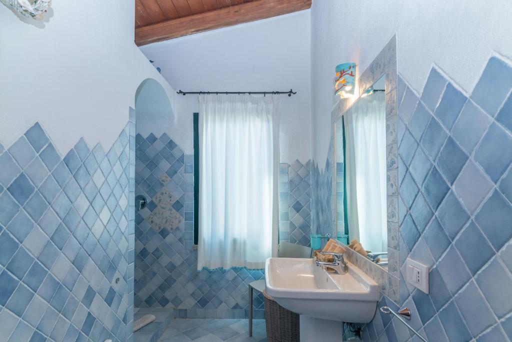 La salle de bains est pourvue de carrelage bleu, d'un lavabo et d'un miroir. dans l'établissement Villa Monte Moro Azzi Russi, à Arzachena 20 autres photos
