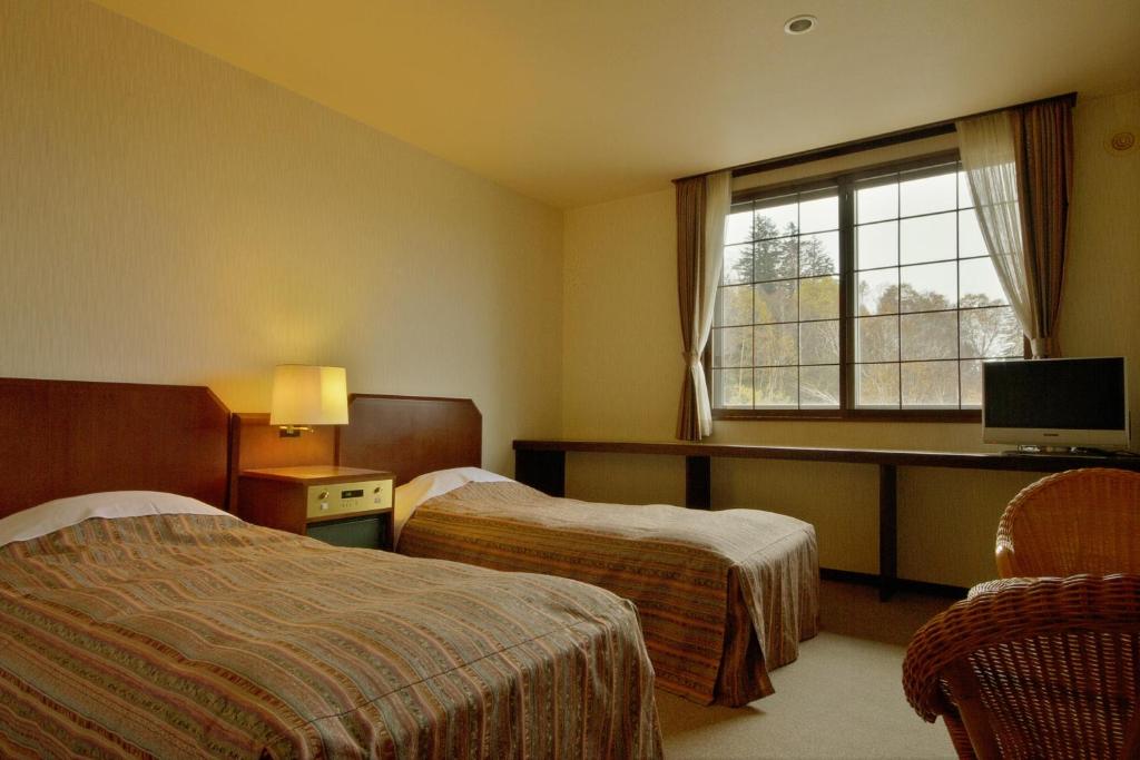 une chambre d'hôtel avec deux lits et une fenêtre dans l'établissement Asahidake Yumoto Yukomanso, à Higashikawa