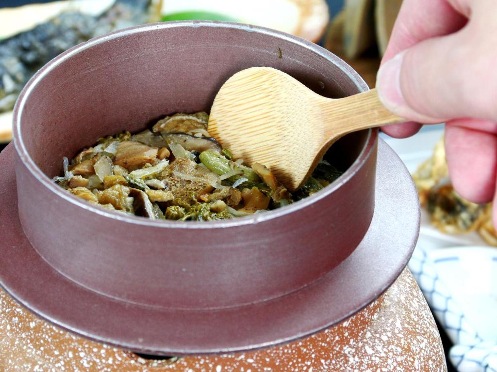 une personne tenant une cuillère en bois dans un pot de nourriture dans l'établissement 富山県 よしのや旅館, à Nanto 37 autres photos