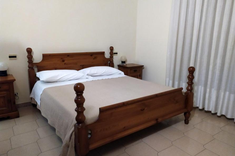 - une chambre dotée d'un lit en bois avec des draps et des oreillers blancs dans l'établissement Hotel Casa Del Gourmet, à Siderno Marina