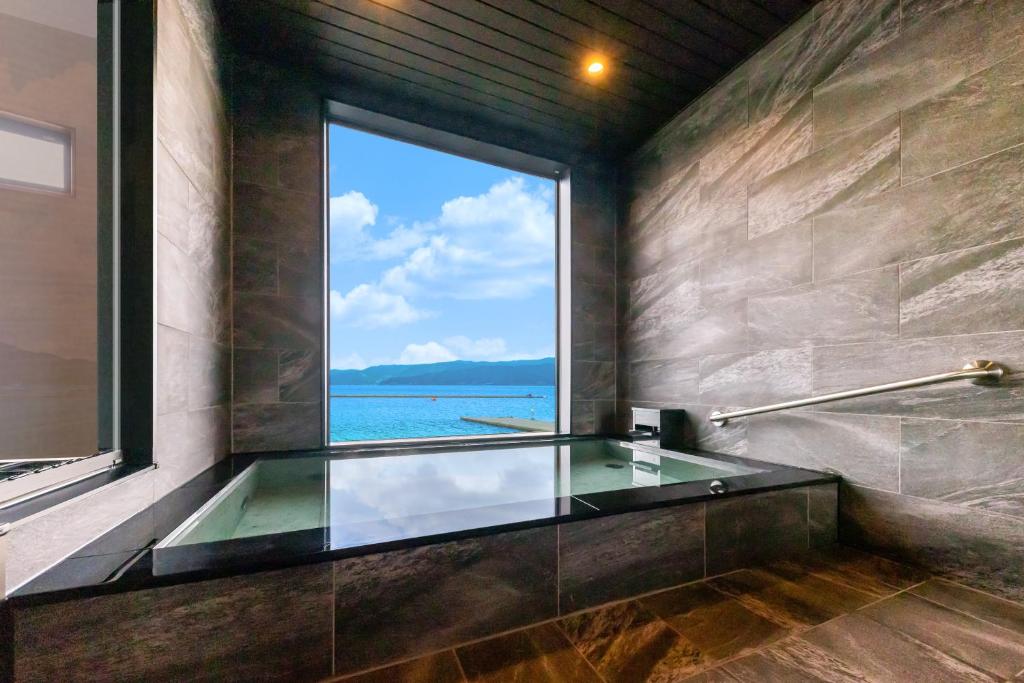 La salle de bains est pourvue d'une baignoire en verre et d'une grande fenêtre. dans l'établissement Tsuruga Sazanami Resort Chobei, à Tsuruga