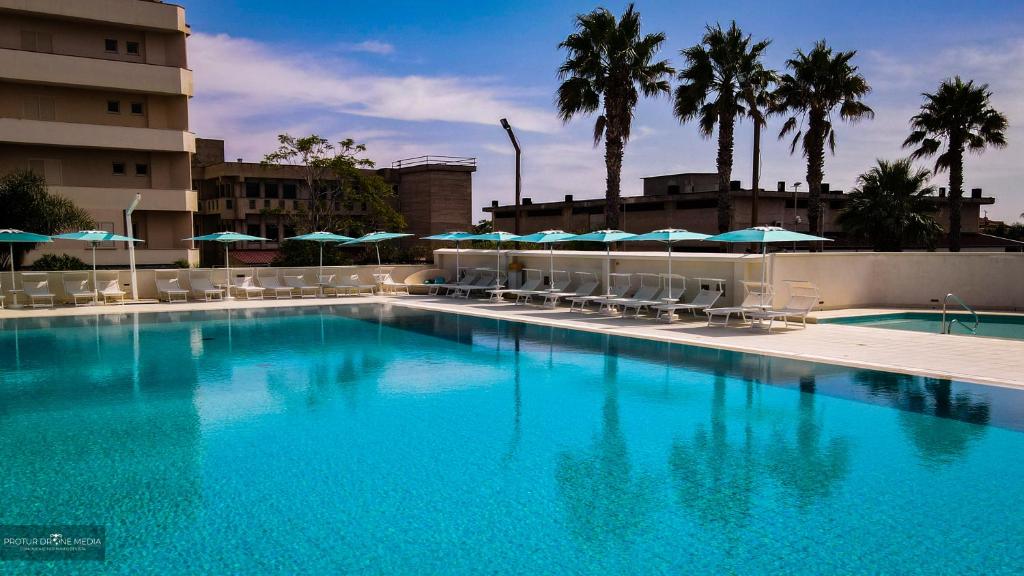 une grande piscine bleue avec chaises et parasols dans l'établissement Grand Hotel President, à Siderno Marina