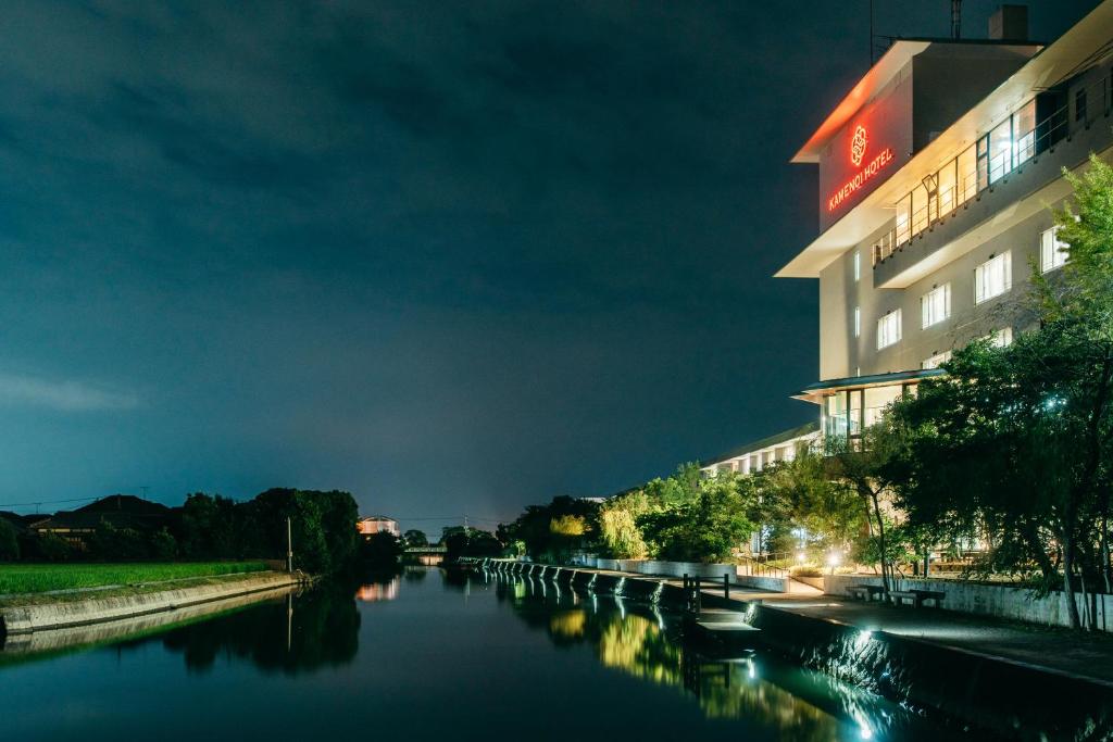 un bâtiment à côté d'une rivière la nuit dans l'établissement KAMENOI HOTEL Yanagawa, à Yanagawa