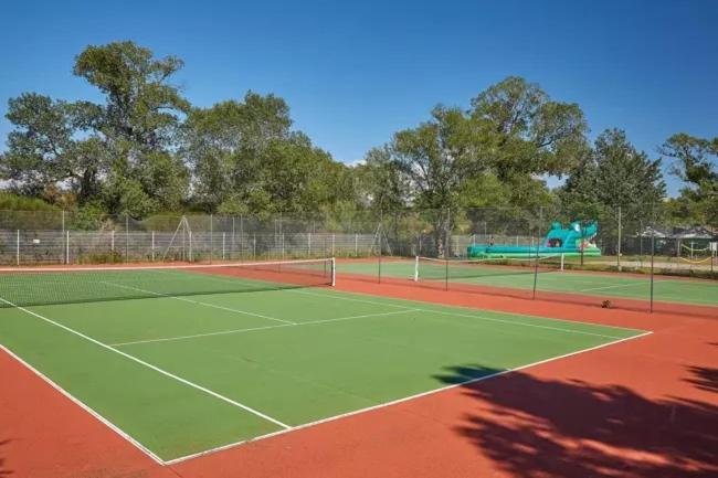 un court de tennis avec une aire de jeux en arrière-plan dans l'établissement mobil home tout confort 6 personnes climatisé au pied du Luberon, à La Roque-dʼAnthéron