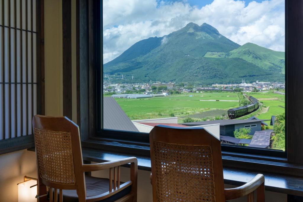 - une vue sur la montagne depuis une fenêtre avec 2 chaises dans l'établissement Yufuin Onsen Toshoan, à Yufu