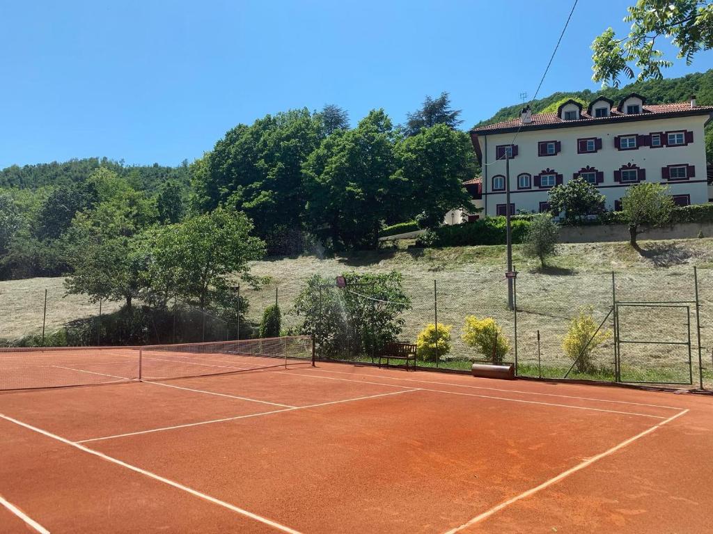un court de tennis avec un bâtiment en arrière-plan dans l'établissement Large villa for 20 guests on large estate with private pool and tennis court Big conference room with facilities VILLAITALY EU, à Cairo Montenotte