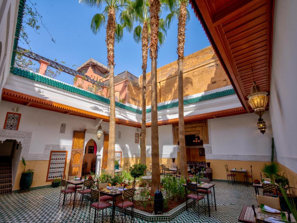 une cour avec des palmiers, des tables et des chaises dans l'établissement Palais Tinmel Marrakech, à Marrakech