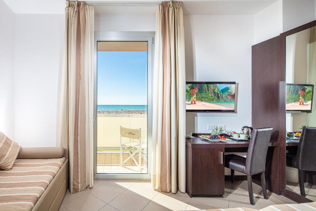 - un salon avec un bureau et une table offrant une vue sur l'océan dans l'établissement Hotel Excelsior, à Bibione