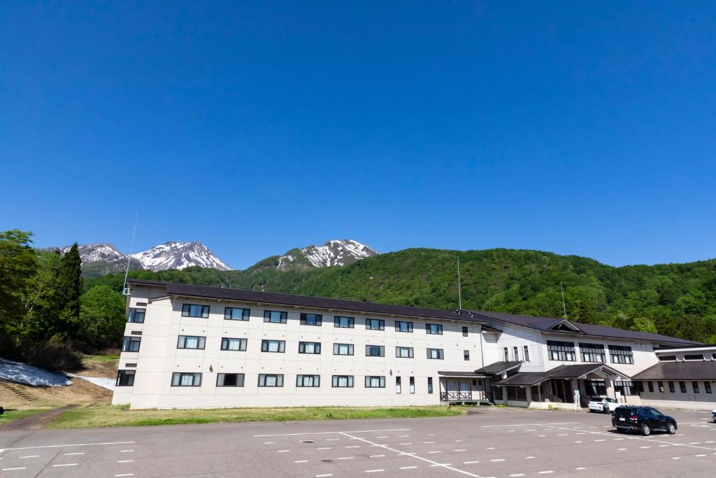 Un grand bâtiment blanc avec des montagnes en arrière-plan dans l'établissement Kyukamura Myoko, à Myōkō