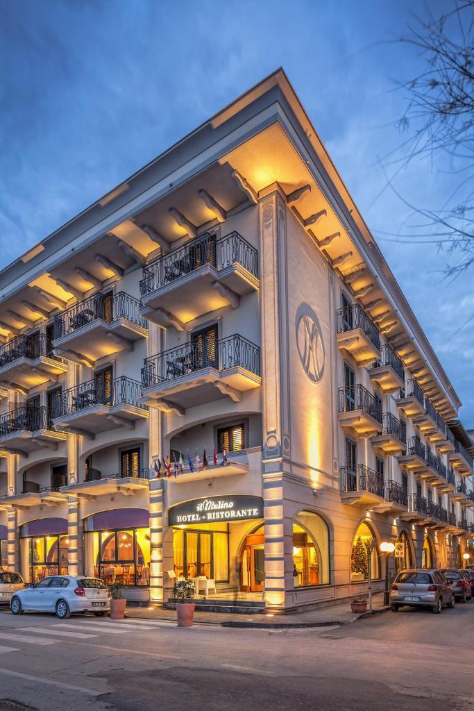 un grand bâtiment avec des voitures garées devant dans l'établissement Hotel Il Mulino, à Capo dʼOrlando
