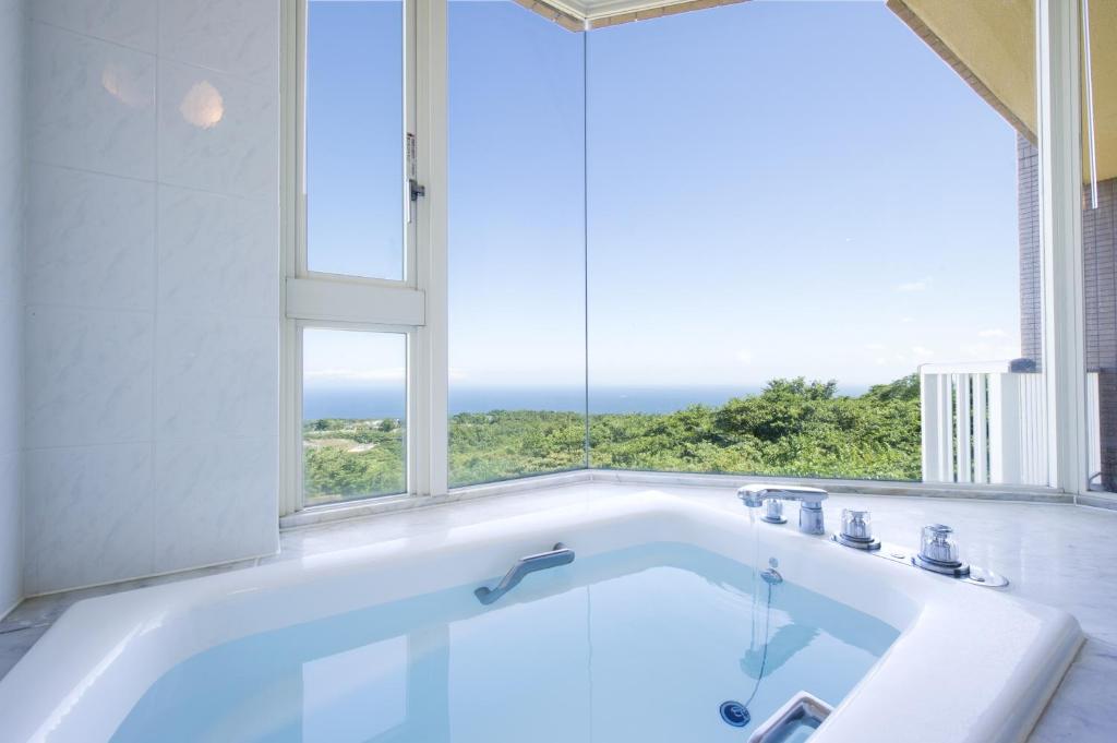 une baignoire dans une salle de bain avec une grande fenêtre dans l'établissement Hotel Village Izukogen, à Itō