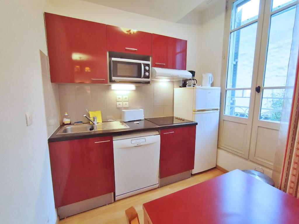 Elle comprend une petite cuisine avec des placards rouges et un réfrigérateur blanc. dans l'établissement Le Marmotton, T2, centre Luchon, wifi, casier à skis, ascenseur, 5 personnes, à Luchon