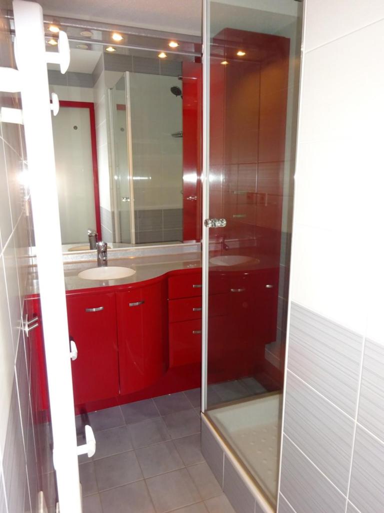 La salle de bains est pourvue de placards rouges et d'une douche en verre. dans l'établissement BIENVENUE AU LIORAN, à Le Lioran