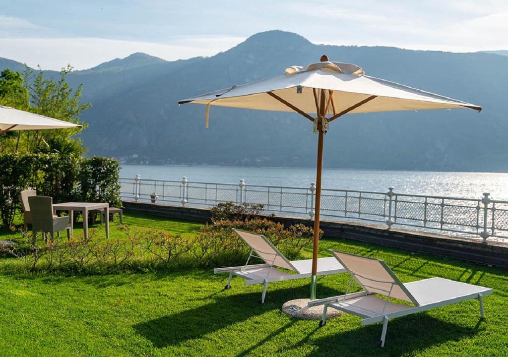 Deux chaises et un parasol sur l'herbe près de l'eau dans l'établissement Villa Lario Resort Mandello, à Mandello del Lario