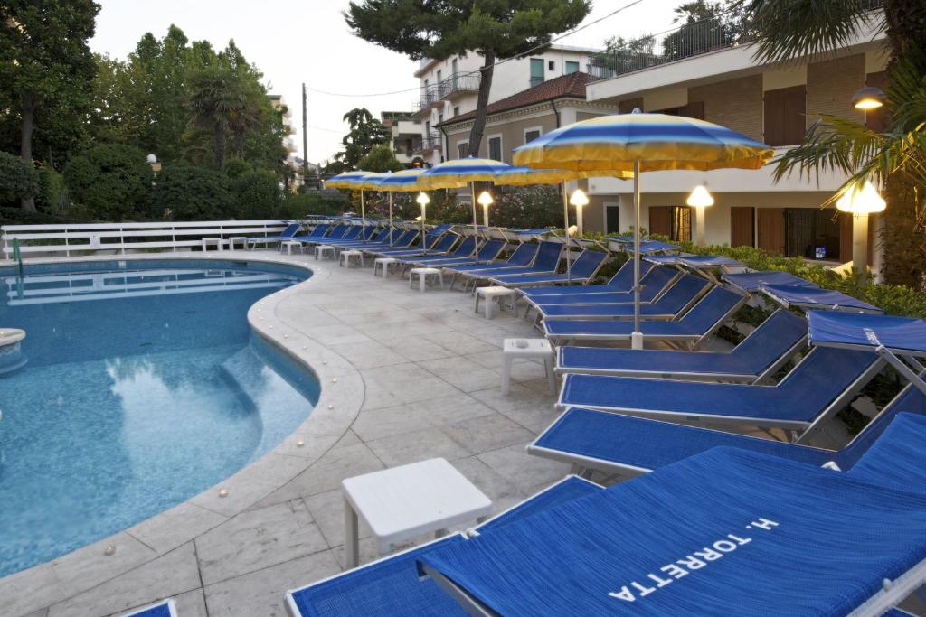 une rangée de chaises bleues et de parasols à côté d'une piscine dans l'établissement Hotel Torretta, à Cattolica