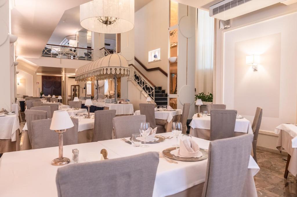 un restaurant avec des tables et des chaises blanches et un escalier dans l'établissement Hotel Anthony, à Lido di Jesolo