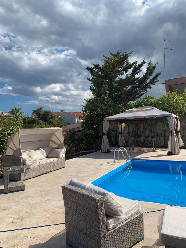 - une piscine avec 2 chaises en osier et un kiosque dans l'établissement LA PERLA BLU DI FONTANE BIANCHE, à Fontane Bianche