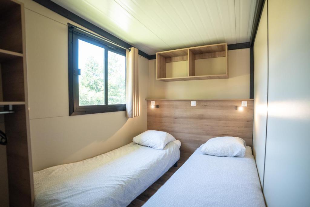 deux lits dans une petite pièce avec une fenêtre dans l'établissement Camping du Sevron, à Saint-Étienne-du-Bois