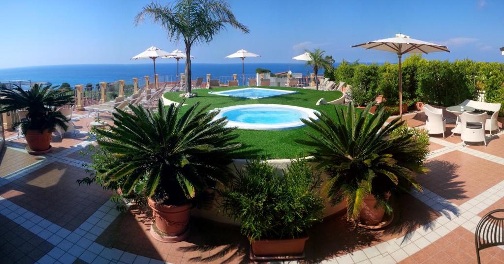 un complexe avec piscine, palmiers et l'océan dans l'établissement Hotel Residence Piccolo, à Parghelia