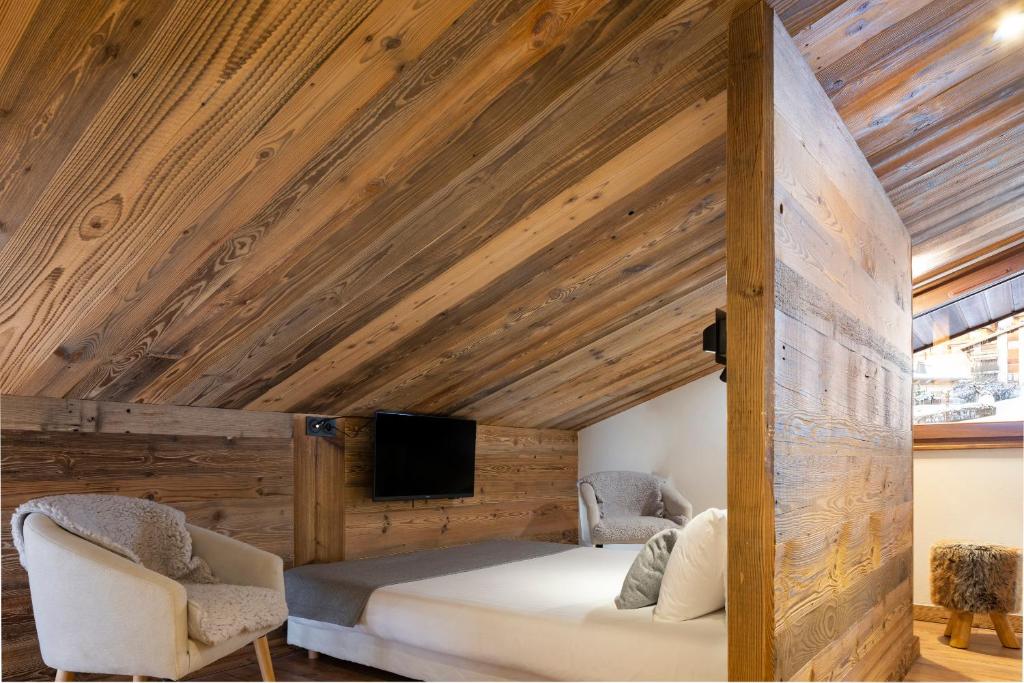 - une chambre dotée d'un plafond en bois avec un lit et deux chaises dans l'établissement Hôtel et Spa Le Vermont, au Grand-Bornand