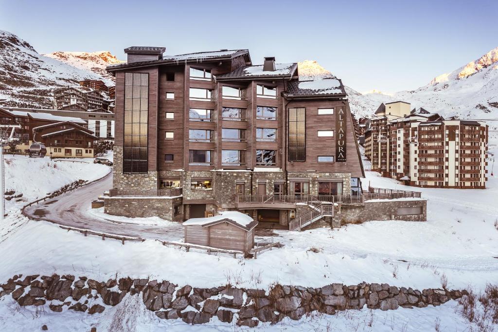 un grand bâtiment dans la neige avec des montagnes en arrière-plan dans l'établissement Altapura Hôtel & Spa Val Thorens, à Val Thorens