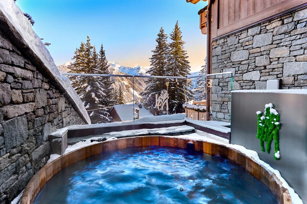 un bain à remous sur le côté d'un bâtiment dans la neige dans l'établissement Lys Martagon, à Courchevel