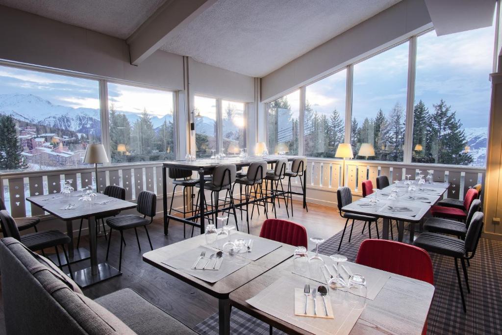 un restaurant avec des tables et des chaises et de grandes fenêtres dans l'établissement Belambra Clubs Arc 1800 - Hôtel Du Golf, à Arc 1800