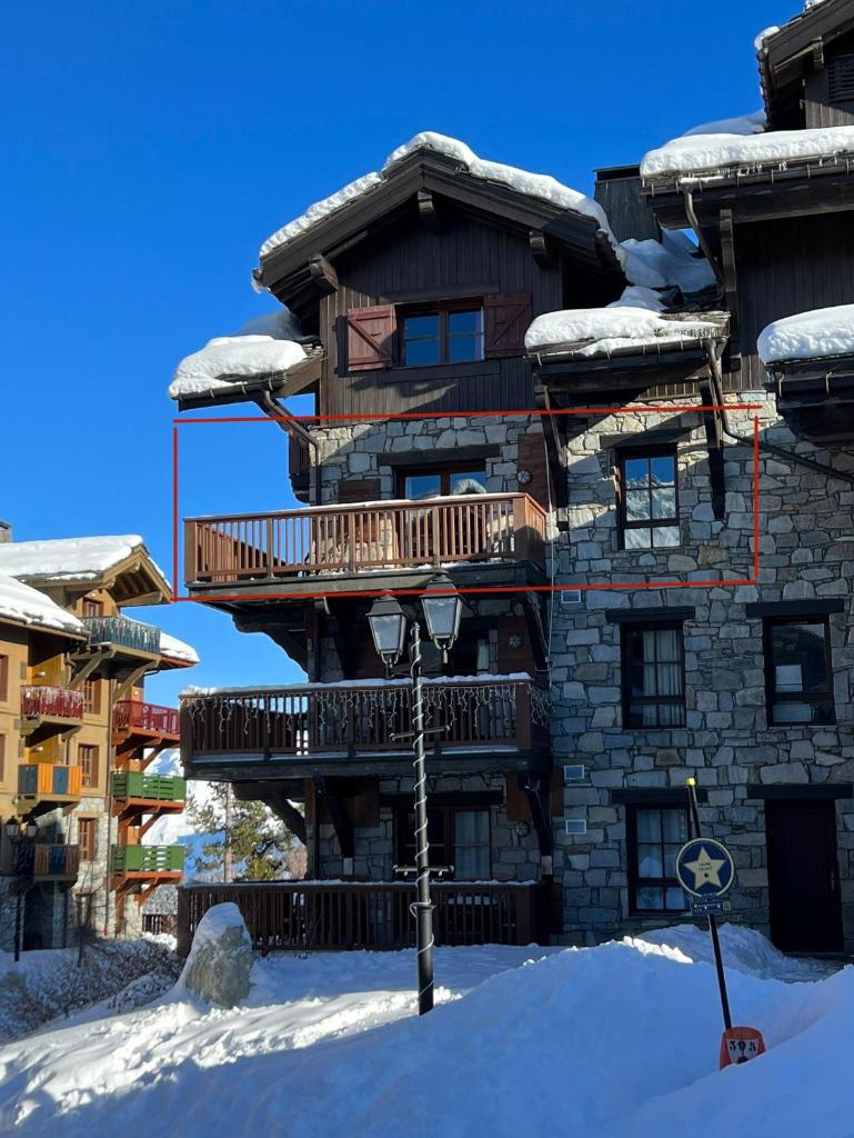 un grand bâtiment avec une terrasse dans la neige dans l'établissement Arc 1950 - Chalet des Lys - appt Luxe 4 pers, à Arc 1950