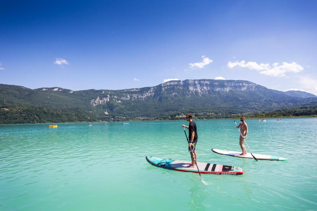 2 personnes sont debout sur des planches de paddle dans l'eau dans l'établissement Huttopia Lac d'Aiguebelette, à Saint-Alban-de-Montbel