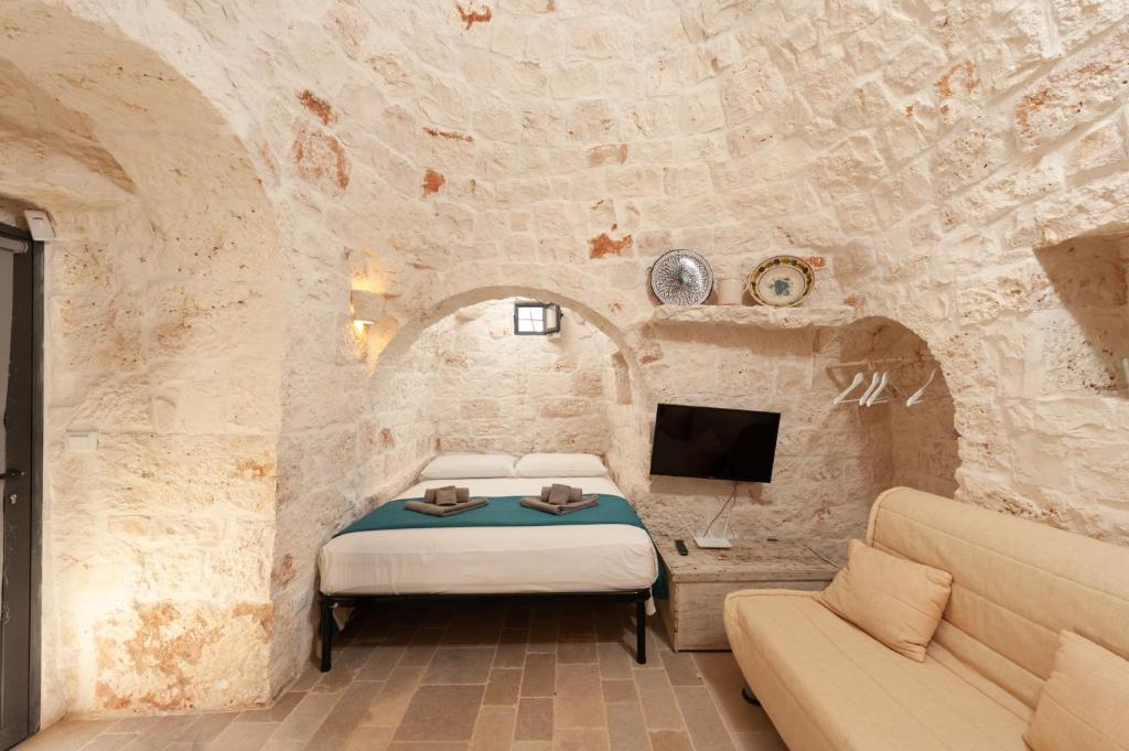 - une chambre avec un lit et une télévision dans un mur en pierre dans l'établissement TRULLI ACQUASALA - Apulian Country Experience, à Ostuni