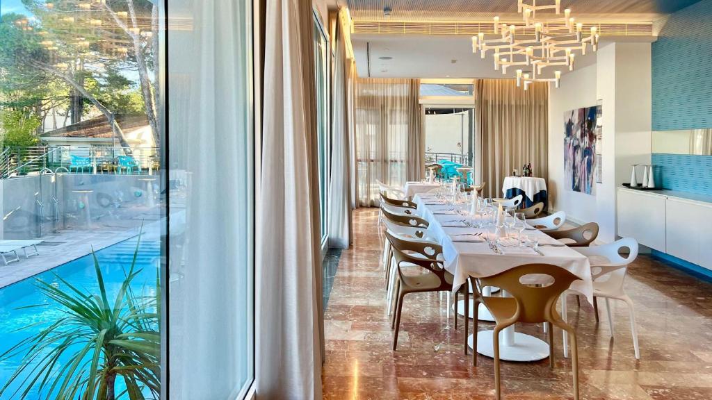 une salle à manger avec une longue table et une piscine dans l'établissement Hotel President, à Lignano Sabbiadoro