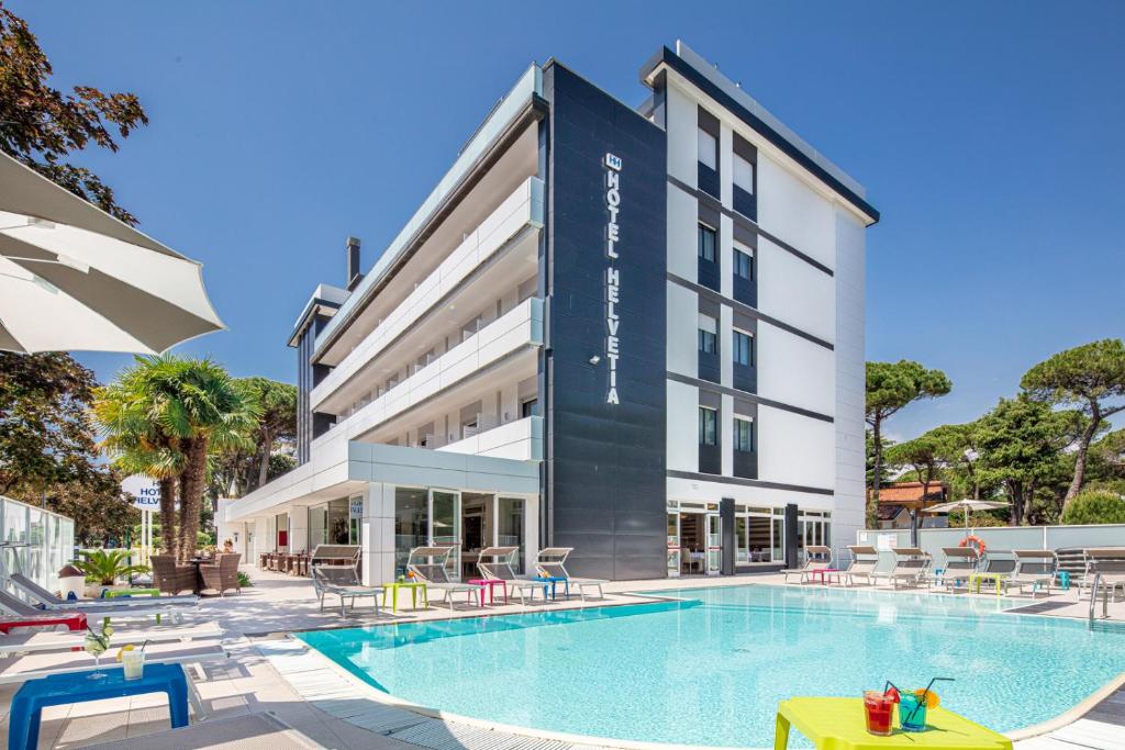 un hôtel avec une piscine devant un bâtiment dans l'établissement Hotel Helvetia, à Lignano Sabbiadoro