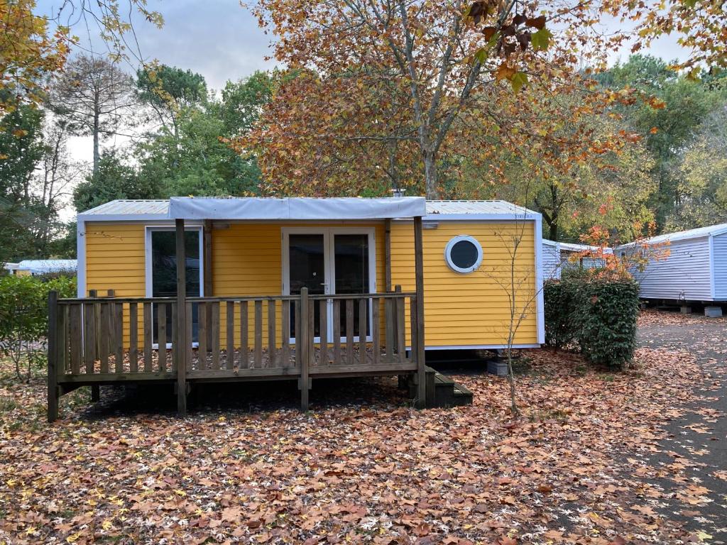 une petite maison jaune avec une terrasse couverte et une terrasse dans l'établissement Camping 5* - Biscarosse Lac - MobilHome 2 chambres - 4 personnes, à Biscarrosse