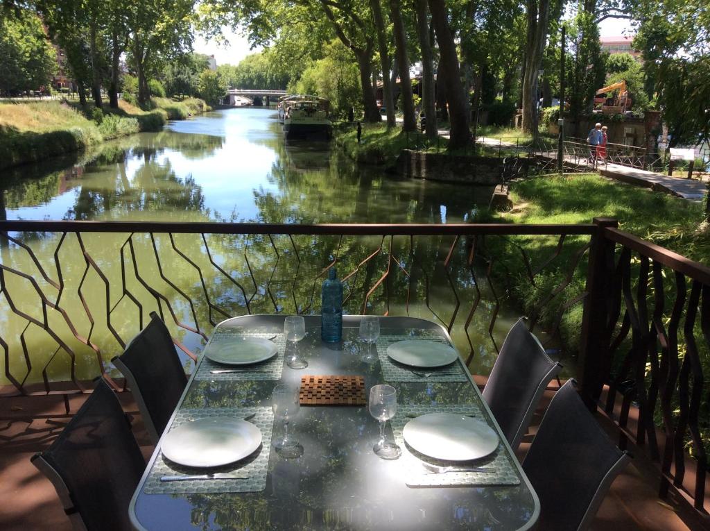- une table avec des chaises et une vue sur la rivière dans l'établissement Péniche Kairos - Havre de paix sur Canal du midi, à Toulouse