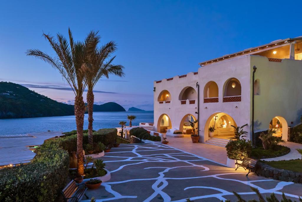 un bâtiment avec un palmier à côté de l'eau dans l'établissement Therasia Resort Sea and SPA - The Leading Hotels of the World, à Vulcano