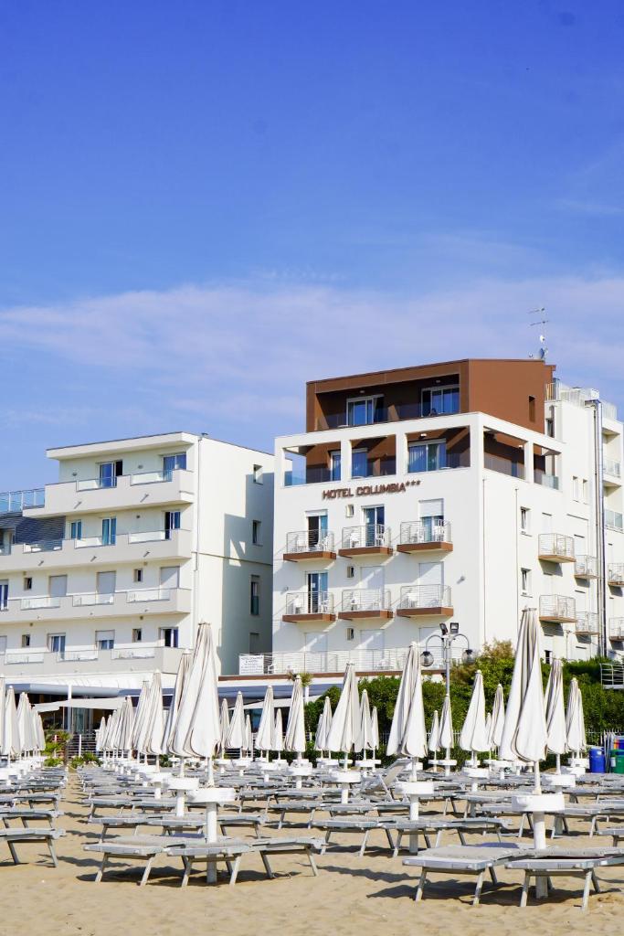 un groupe de chaises et de parasols devant un bâtiment dans l'établissement Hotel Columbia & Ninfea, à Lido di Jesolo