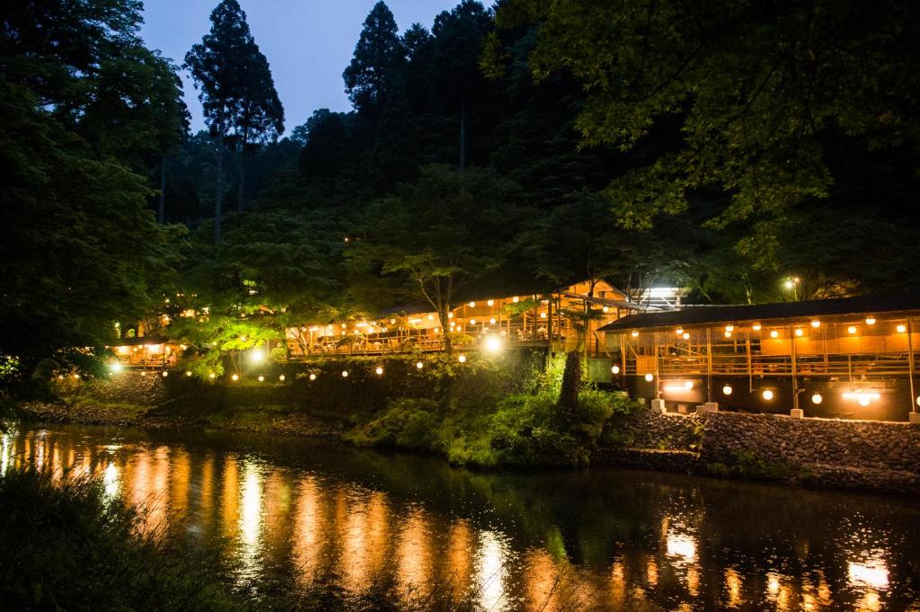 un bâtiment éclairé à côté d'une rivière la nuit dans l'établissement Momijiya Honkan Takaosansou, à Kyoto