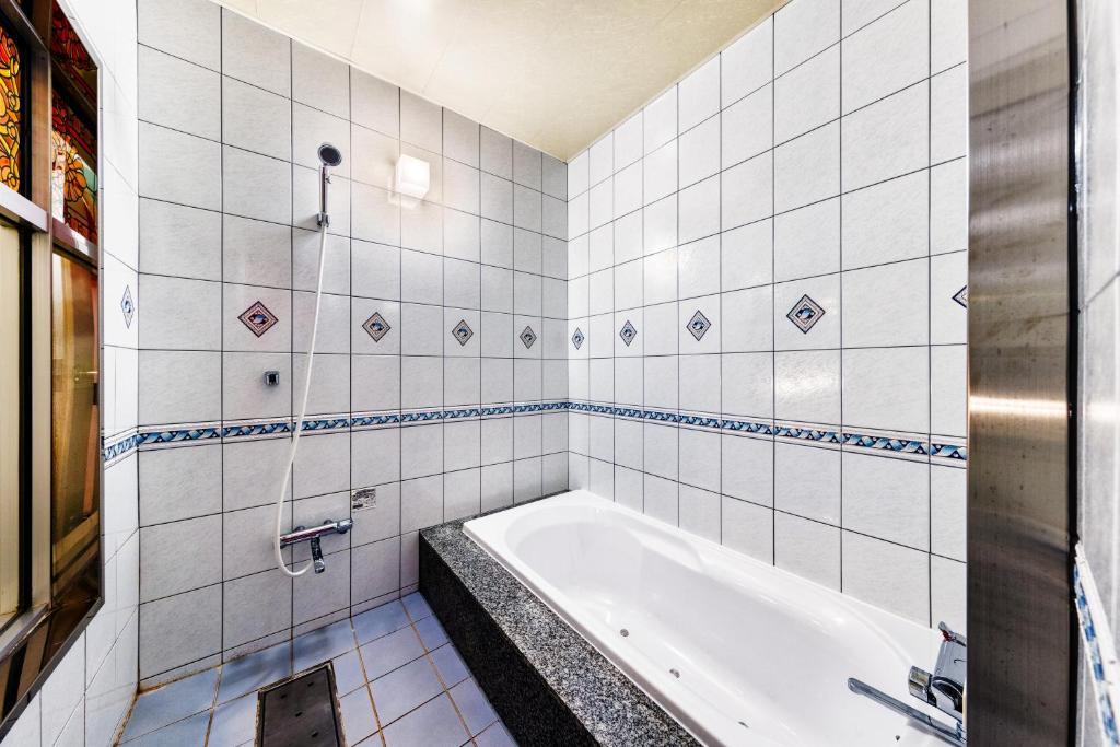 La salle de bains est pourvue de carrelage blanc et d'une baignoire. dans l'établissement Hotel Chronos -Adult Only, à Fushimi