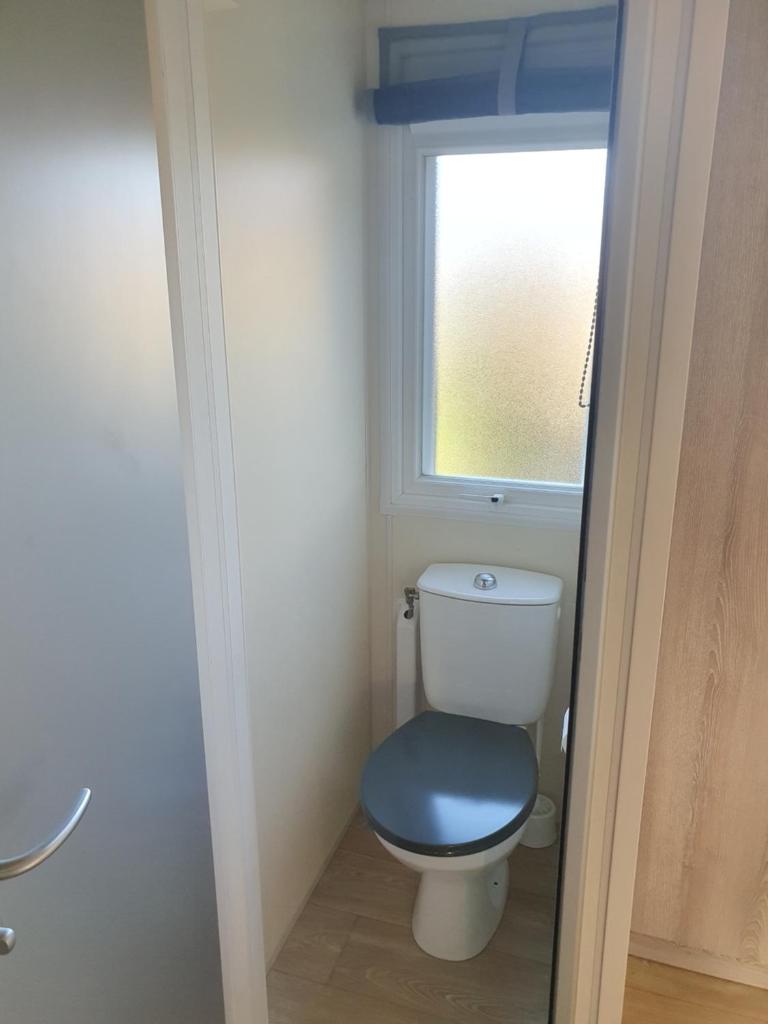 La salle de bains est pourvue de toilettes avec un siège bleu et une fenêtre. dans l'établissement Charmant mobil-home, à Rocbaron 14 autres photos