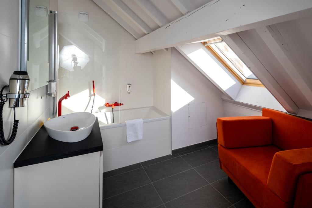 une salle de bains mansardée avec une chaise orange et un lavabo dans l'établissement PopAlp, à L'Alpe-d'Huez 37 autres photos