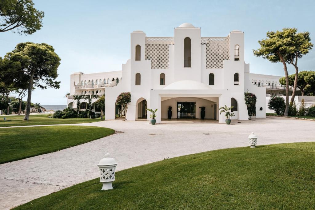 un grand bâtiment blanc avec une cour herbeuse dans l'établissement Falkensteiner Resort Capo Boi, à Villasimius