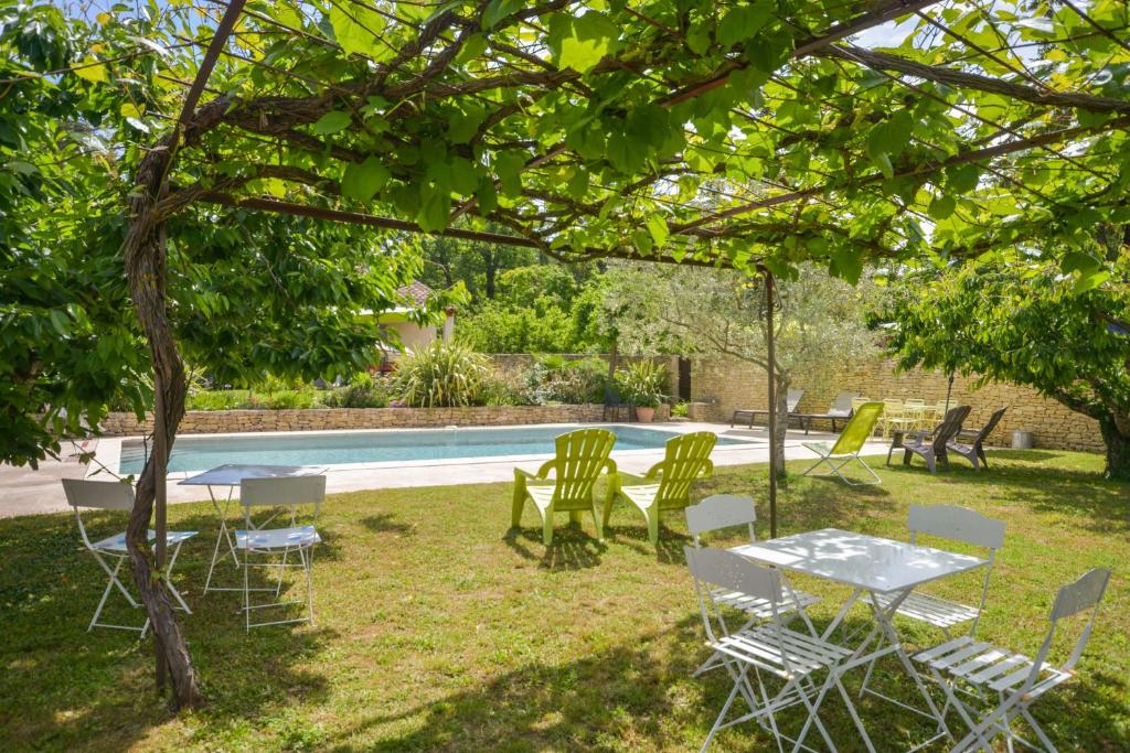 un groupe de chaises et de tables sous un arbre près d'une piscine dans l'établissement Gîte La loge 142 route de CARPENTRAS 84210 VENASQUE, à Venasque