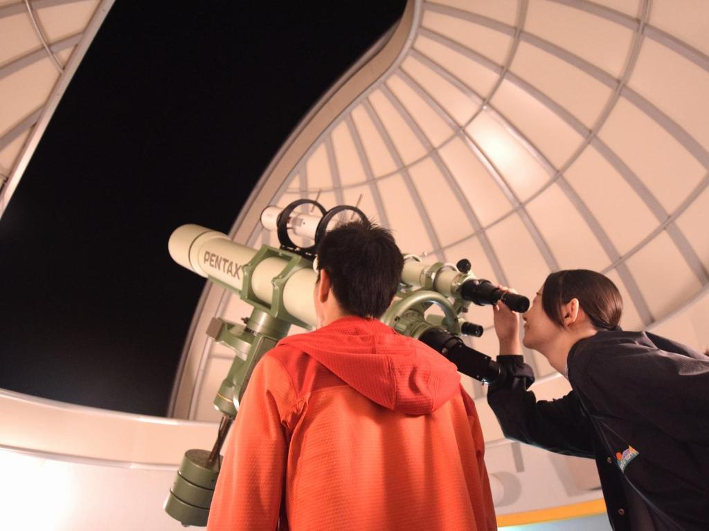 deux personnes regardant dans un télescope dans une pièce dans l'établissement Kyukamura Noto-Chirihama, à Hakui 22 autres photos