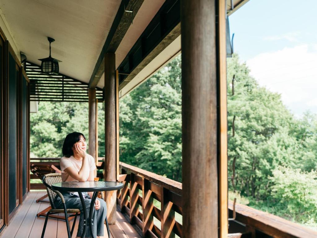 une femme assise à une table sur un porche dans l'établissement 津川温泉 清川高原保養センター, à Aga